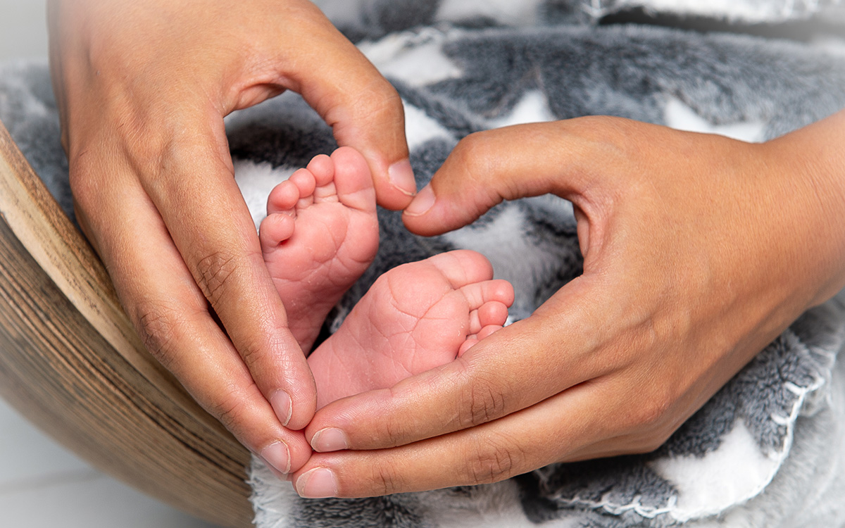 Bild einer Mama, die mit ihren Händen ein Herz um die Füße ihres Babys formt.