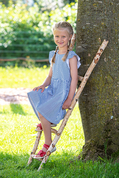 Mädchen steht auf einer Leiter aus Holz.