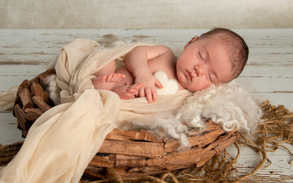 Ein in einem Korb schlafendes Neugeborenes mit einem Herz im Arm