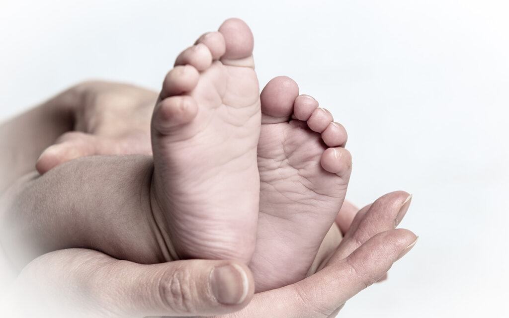 Füße eines Babys, die von den Händen der Mutter gehalten werden. 